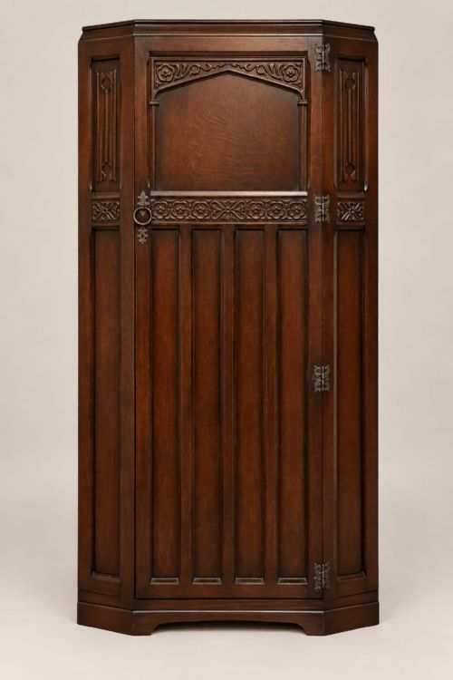 fig 2. A dark oak single-door wardrobe featuring carved floral band detailing, an arched upper panel, vertical linear panelling, and iron hardware.