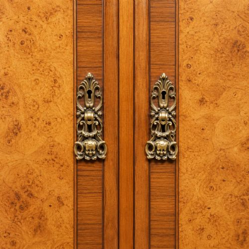 fig 2. An antique circa 1920 burr walnut triple wardrobe featuring three panelled doors with figured wood grain, carved top cresting, and carved cabriole feet.