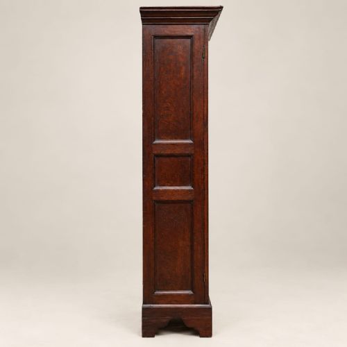 fig 2. A tall dark oak George III cupboard featuring two panelled doors decorated with carved lunettes, rosettes, and geometric motifs, standing on bracket feet.