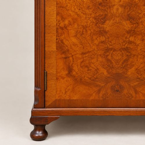 fig 1. A two-door 1920s small burr walnut wardrobe featuring symmetrical bookmatched wood grain, a gently arched top, brass drop handles, and short turned feet.