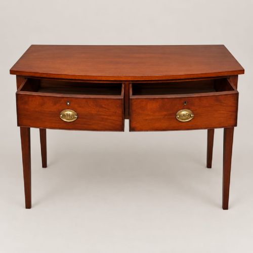 fig 2. A Regency mahogany bow-fronted side table featuring two drawers with brass handles and supported by four tapered legs.