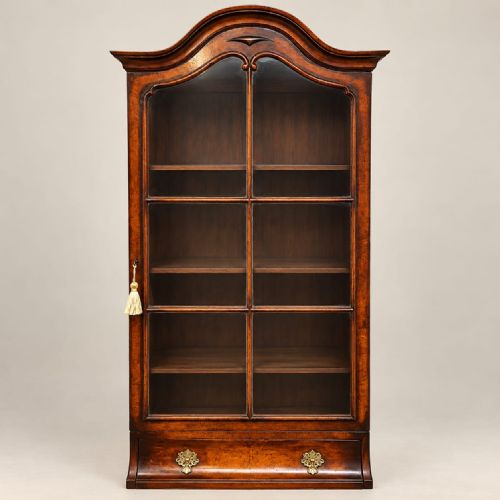 fig 1. A tall, narrow burr walnut cabinet featuring an arched glazed upper section above three drawers supported by slender cabriole legs.