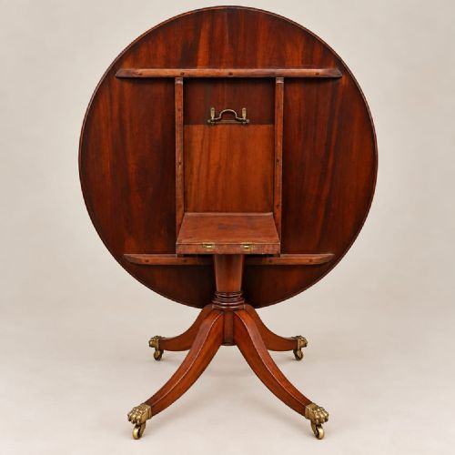 fig 1. A circular mahogany dining table featuring a polished timber surface and a central pedestal with four splayed legs terminating in brass lion paw castors.