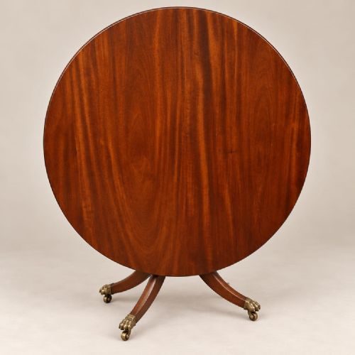 fig 2. A circular mahogany dining table featuring a polished timber surface and a central pedestal with four splayed legs terminating in brass lion paw castors.