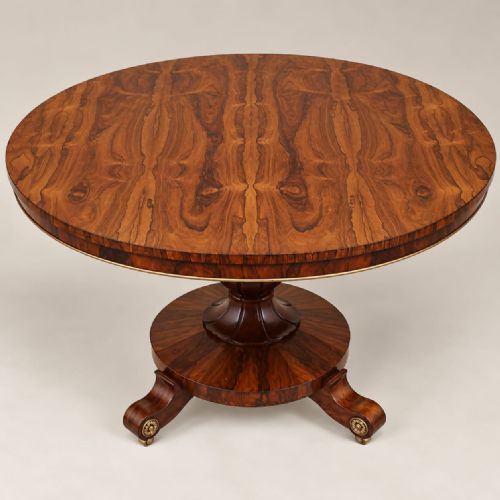 fig 1. A circular William IV rosewood dining table featuring book-matched veneer on top, supported by a central column stem and a circular plinth base with scroll feet.