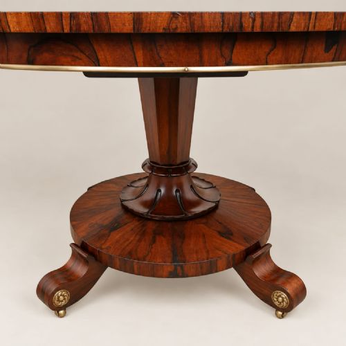 fig 2. A circular William IV rosewood dining table featuring book-matched veneer on top, supported by a central column stem and a circular plinth base with scroll feet.