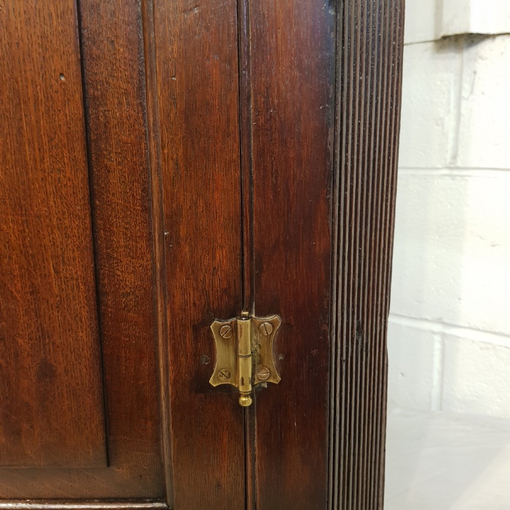 An 18th-century dark oak wall-hanging corner cabinet featuring a single panelled door with brass H-hinges and a keyhole escutcheon, topped with a dentil moulded cornice. View III