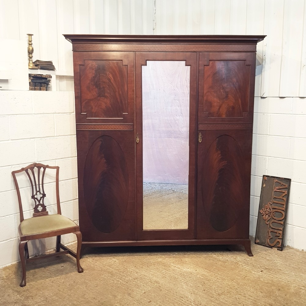 A late Victorian rich mahogany triple wardrobe featuring a central full-length mirrored door flanked by two flame mahogany panelled doors topped by a classical cornice.
