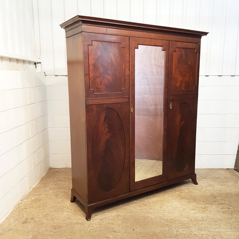 A late Victorian rich mahogany triple wardrobe featuring a central full-length mirrored door flanked by two flame mahogany panelled doors topped by a classical cornice. View III