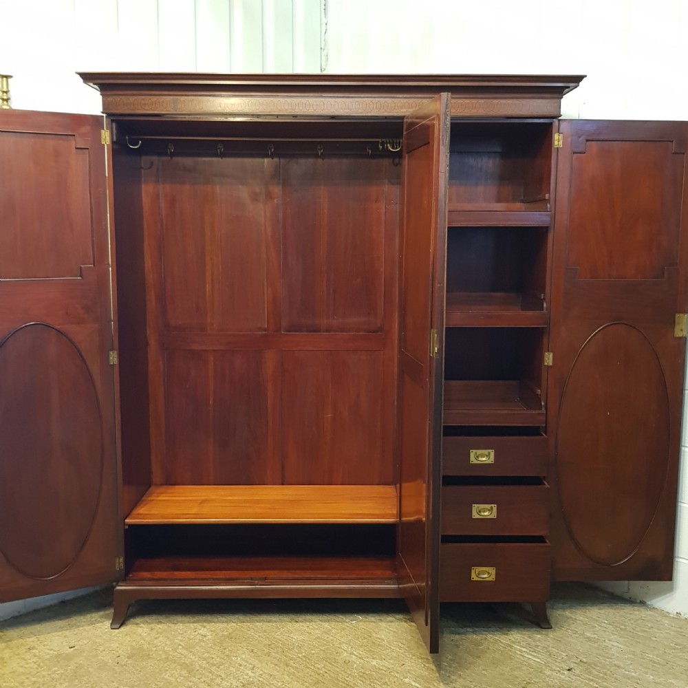 A late Victorian rich mahogany triple wardrobe featuring a central full-length mirrored door flanked by two flame mahogany panelled doors topped by a classical cornice. View VII