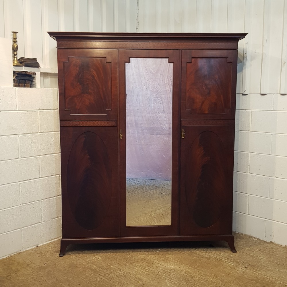 A late Victorian rich mahogany triple wardrobe featuring a central full-length mirrored door flanked by two flame mahogany panelled doors topped by a classical cornice. View VIII