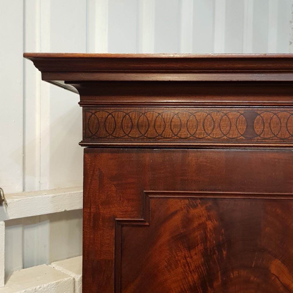 A late Victorian rich mahogany triple wardrobe featuring a central full-length mirrored door flanked by two flame mahogany panelled doors topped by a classical cornice. View IX