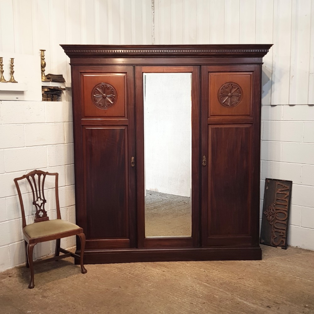 A late Victorian dark mahogany triple wardrobe featuring a central full-length mirror flanked by two timber panel doors with carved circular rosettes.