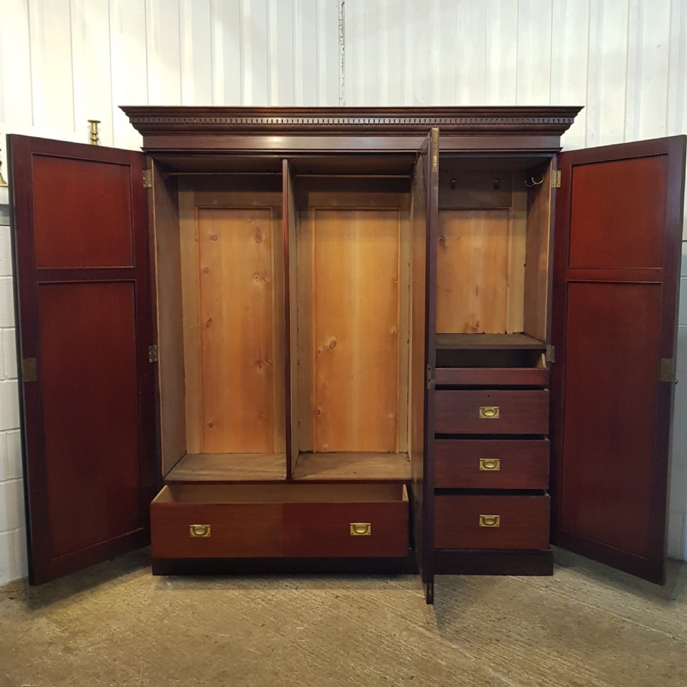 A late Victorian dark mahogany triple wardrobe featuring a central full-length mirror flanked by two timber panel doors with carved circular rosettes. View II