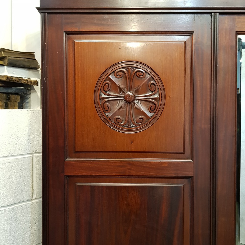 A late Victorian dark mahogany triple wardrobe featuring a central full-length mirror flanked by two timber panel doors with carved circular rosettes. View III