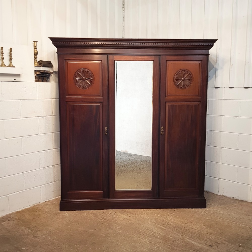 A late Victorian dark mahogany triple wardrobe featuring a central full-length mirror flanked by two timber panel doors with carved circular rosettes. View VI