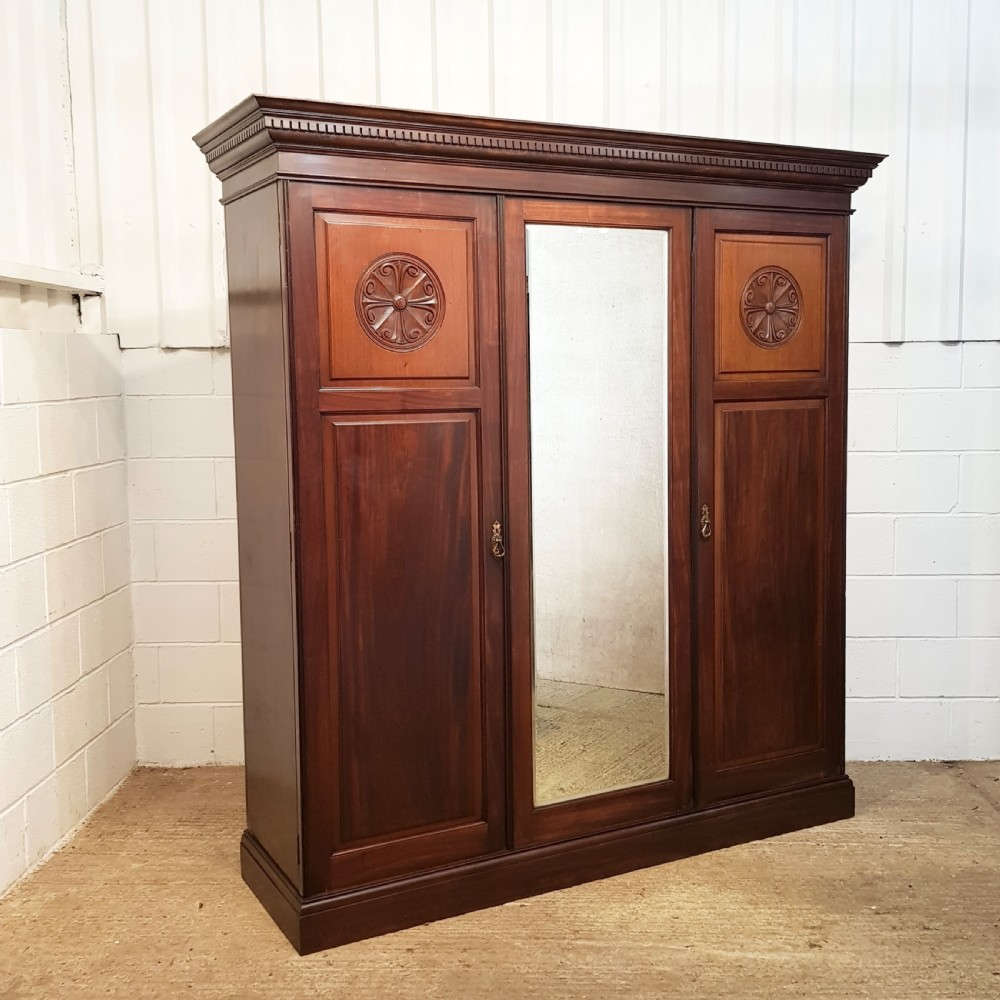 A late Victorian dark mahogany triple wardrobe featuring a central full-length mirror flanked by two timber panel doors with carved circular rosettes. View VII
