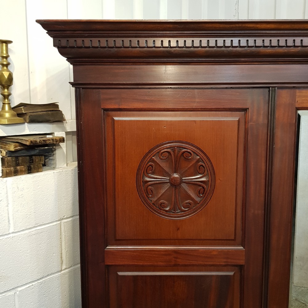 A late Victorian dark mahogany triple wardrobe featuring a central full-length mirror flanked by two timber panel doors with carved circular rosettes. View VIII