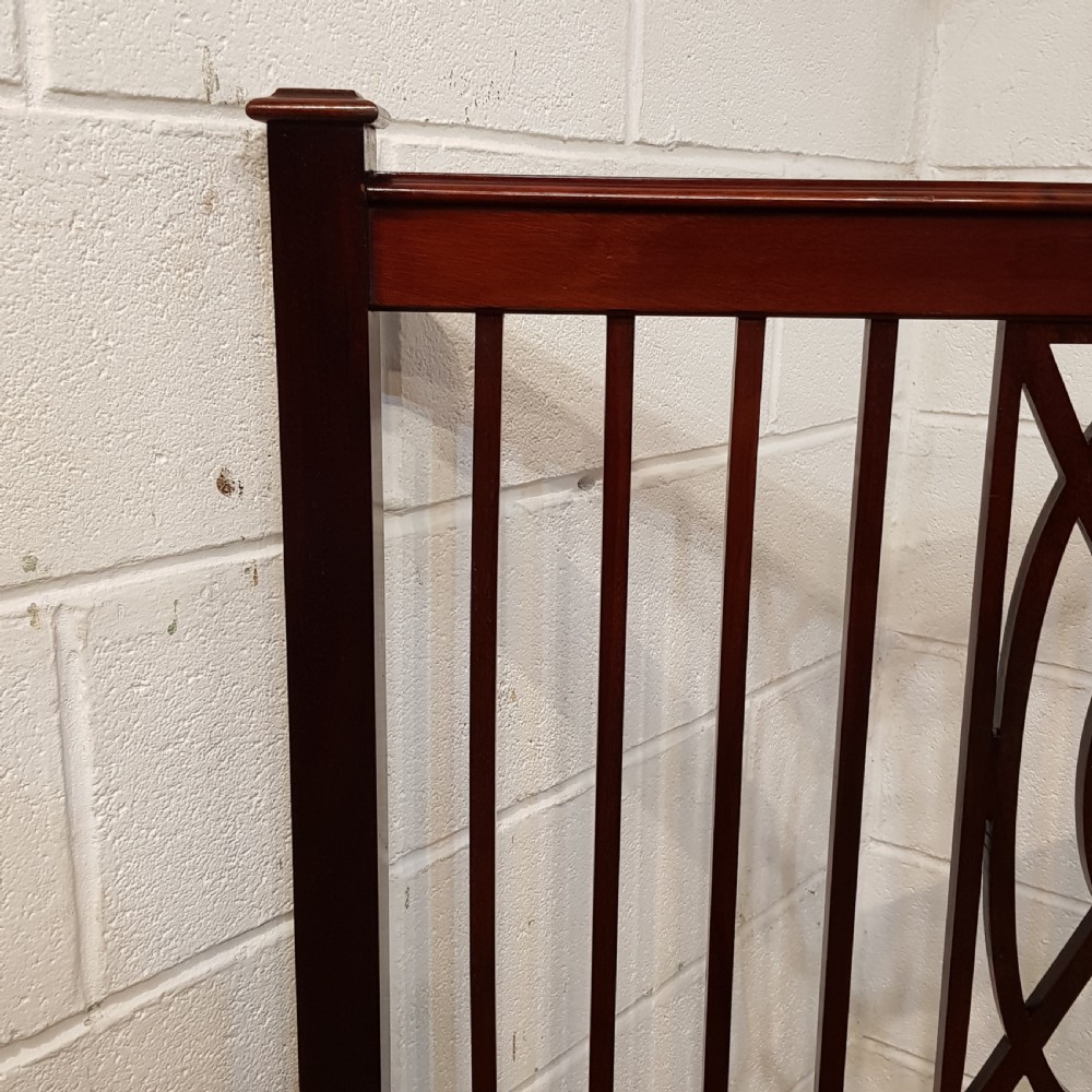 A pair of Edwardian mahogany single bed frames featuring slatted headboards and footboards accented with central geometric oval motifs and standing on castors. View II