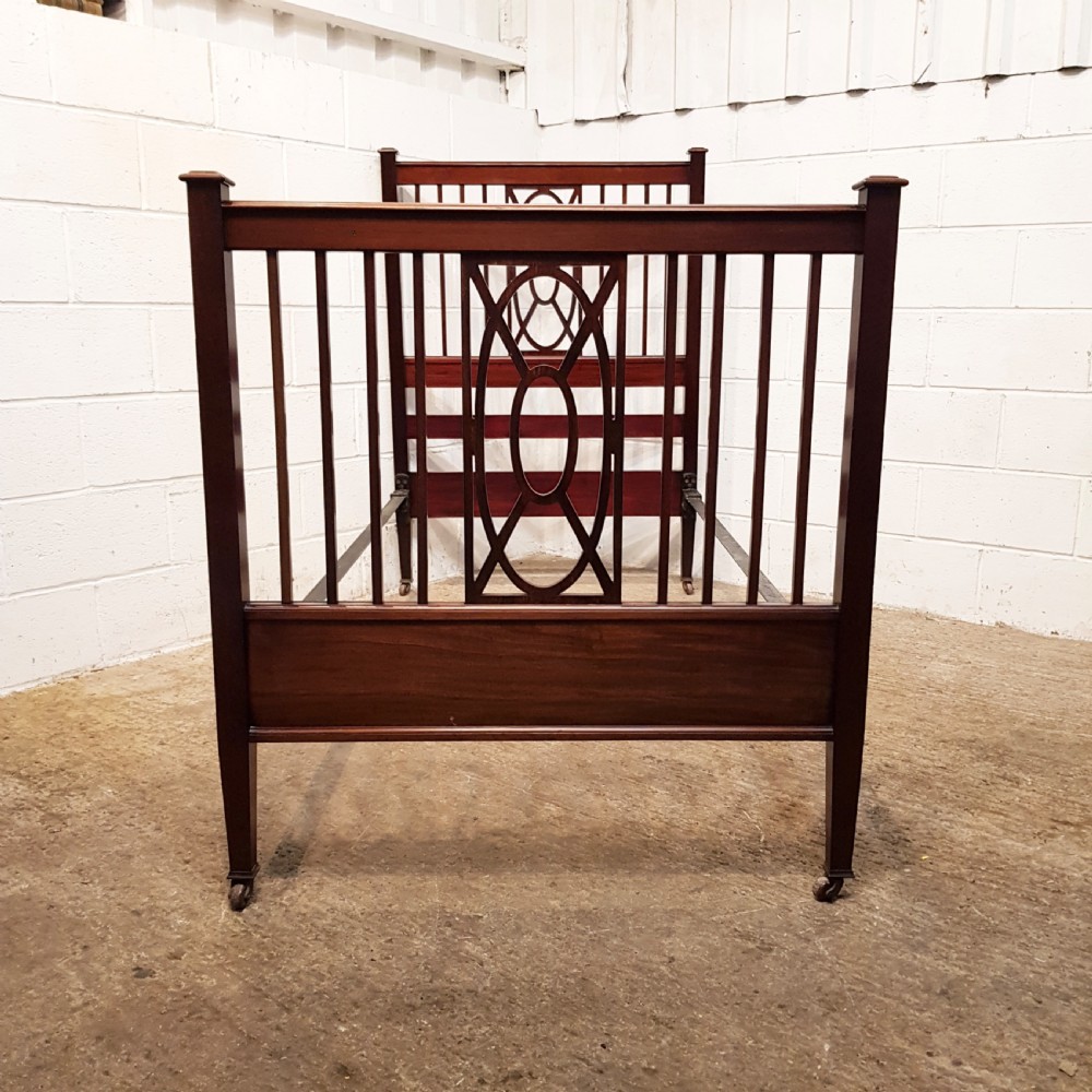 A pair of Edwardian mahogany single bed frames featuring slatted headboards and footboards accented with central geometric oval motifs and standing on castors. View III