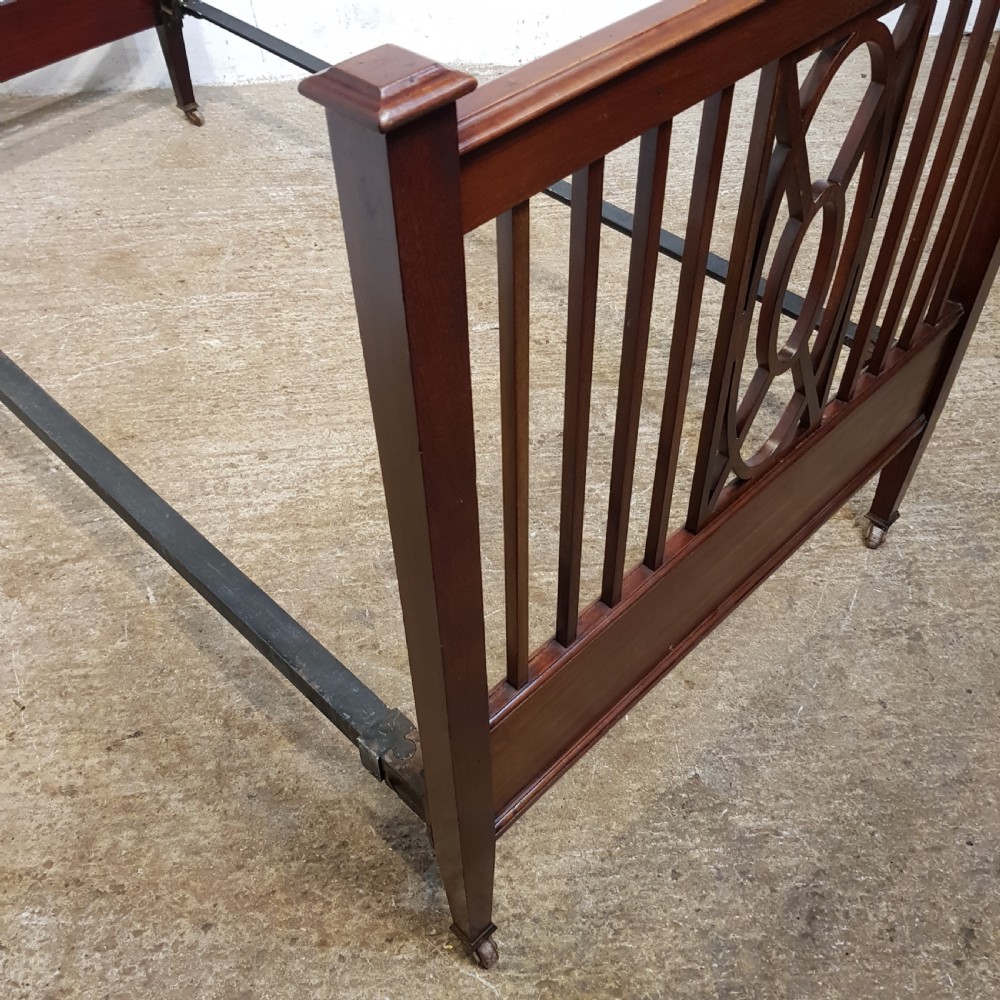 A pair of Edwardian mahogany single bed frames featuring slatted headboards and footboards accented with central geometric oval motifs and standing on castors. View V