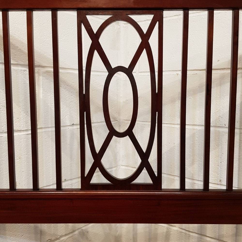A pair of Edwardian mahogany single bed frames featuring slatted headboards and footboards accented with central geometric oval motifs and standing on castors. View VI