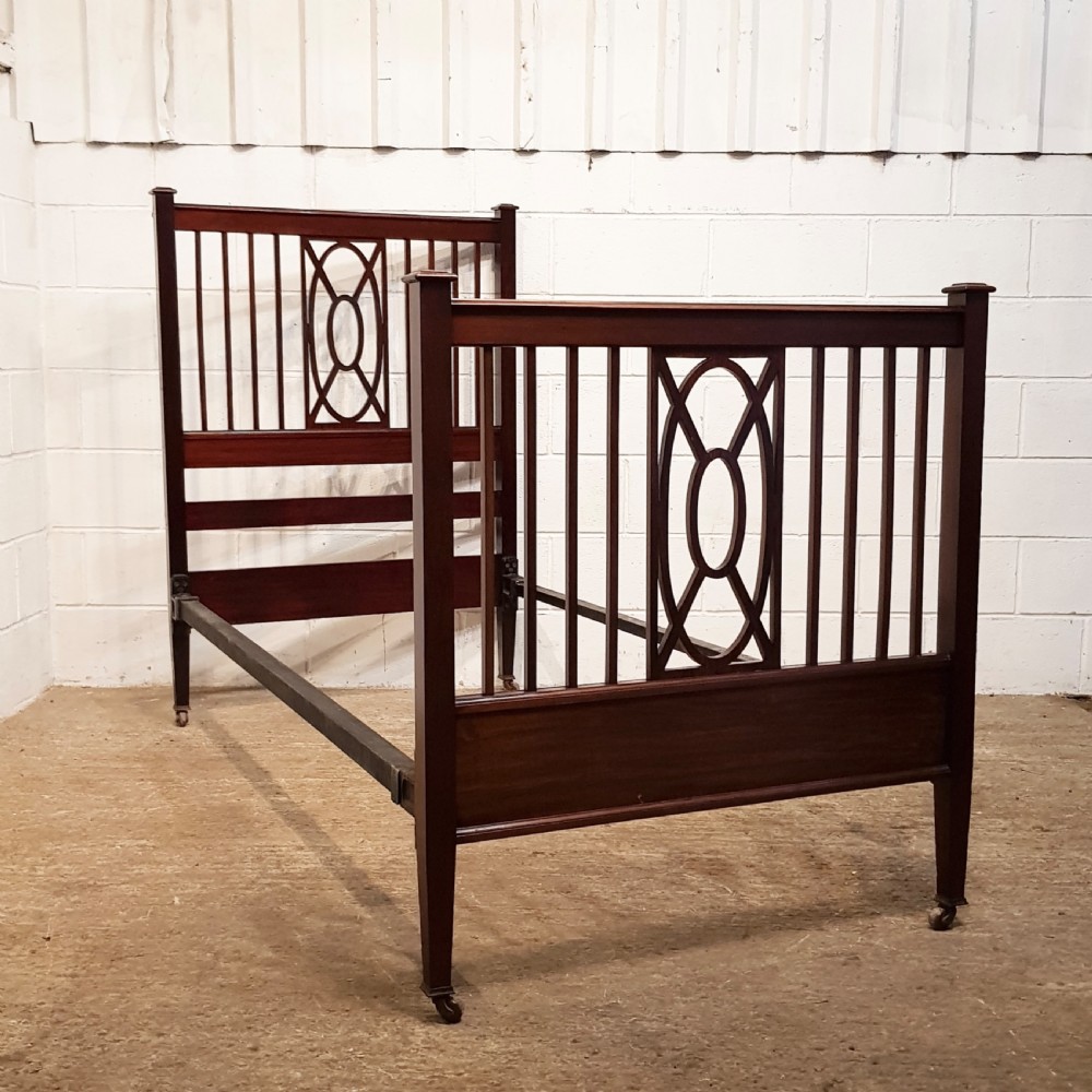 A pair of Edwardian mahogany single bed frames featuring slatted headboards and footboards accented with central geometric oval motifs and standing on castors. View VII