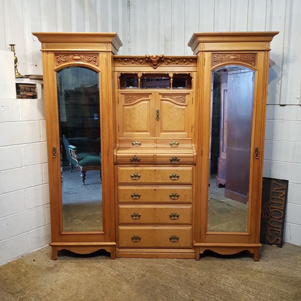An antique Victorian satin walnut and maple combination wardrobe featuring two tall outer sections with mirrored doors flanking a central chest of drawers and small upper cupboard.