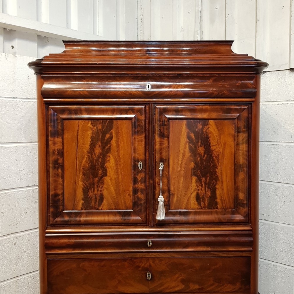 A nineteenth-century Biedermeier flame mahogany tall storage cabinet featuring double upper doors with figure-matched veneer and three full-width lower drawers. View XII