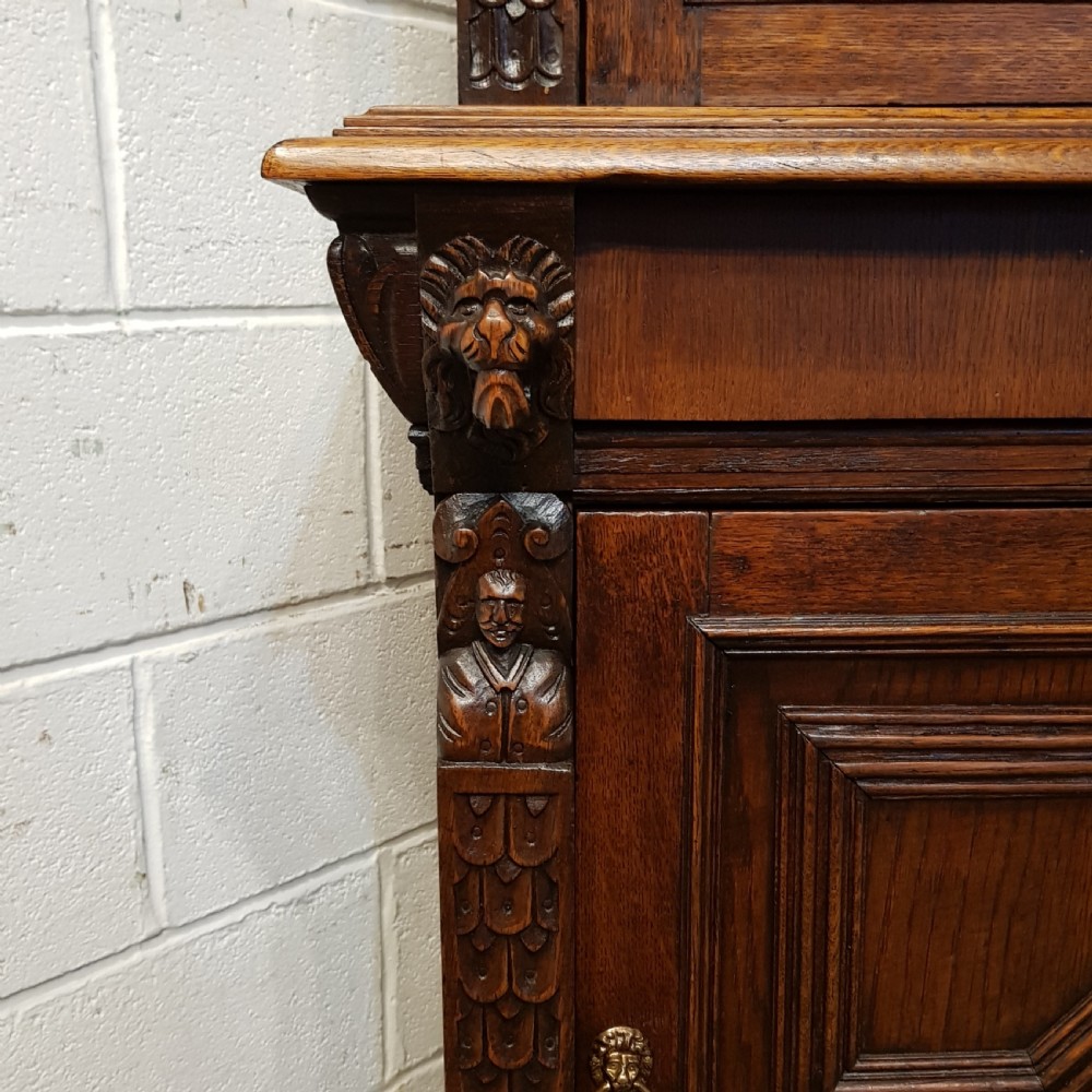 A tall, narrow Victorian Gothic carved oak bookcase cabinet featuring a single glazed door above a geometric panelled lower cupboard door. View V