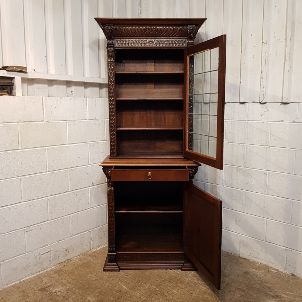A tall, narrow Victorian Gothic carved oak bookcase cabinet featuring a single glazed door above a geometric panelled lower cupboard door. View VII