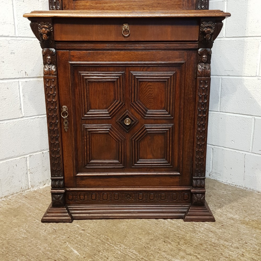 A tall, narrow Victorian Gothic carved oak bookcase cabinet featuring a single glazed door above a geometric panelled lower cupboard door. View IX