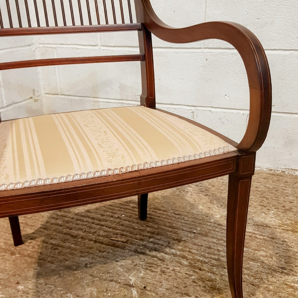 A pair of Edwardian mahogany armchairs featuring inlaid marquetry backsplats, vertical spindles, sweeping armrests, and striped fabric upholstery. View IX