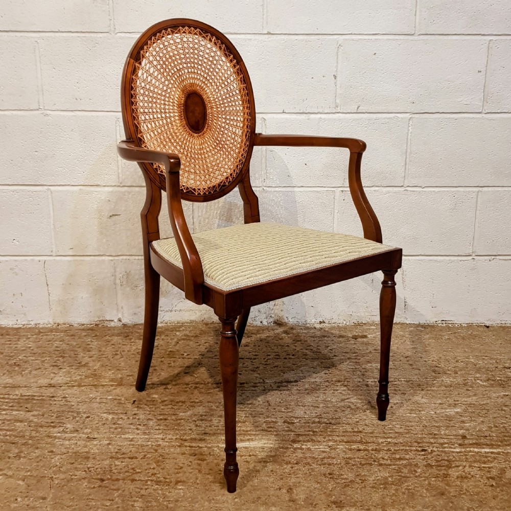 A mahogany armchair featuring an oval woven cane back with a central timber medallion, curved armrests, and turned front legs.