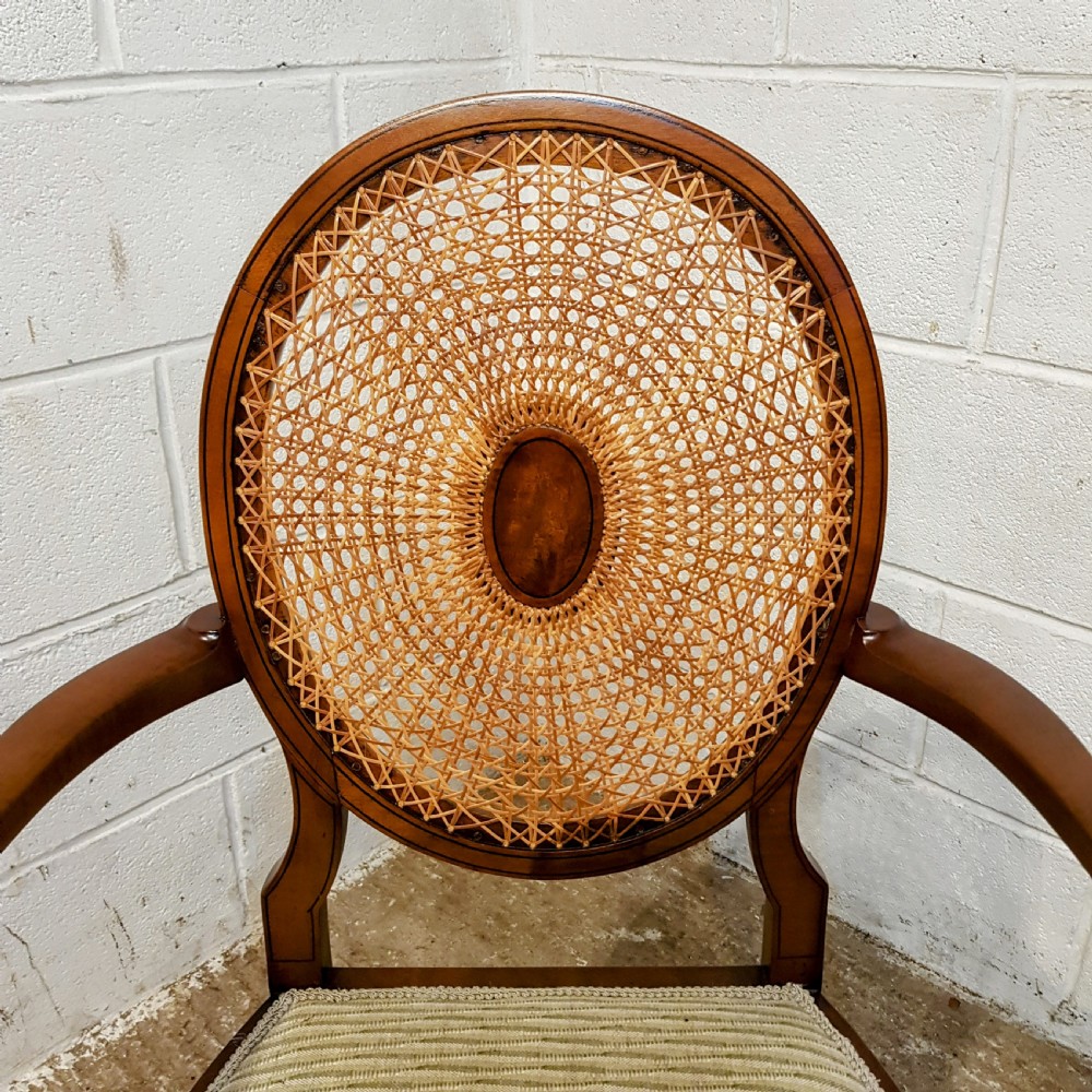 A mahogany armchair featuring an oval woven cane back with a central timber medallion, curved armrests, and turned front legs. View VI