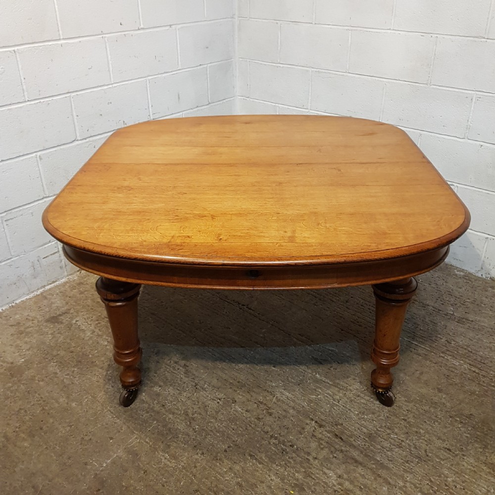 AN ANTIQUE VICTORIAN OAK EXTENDING WIND OUT DINING TABLE WITH TWO EXTRA LEAVES