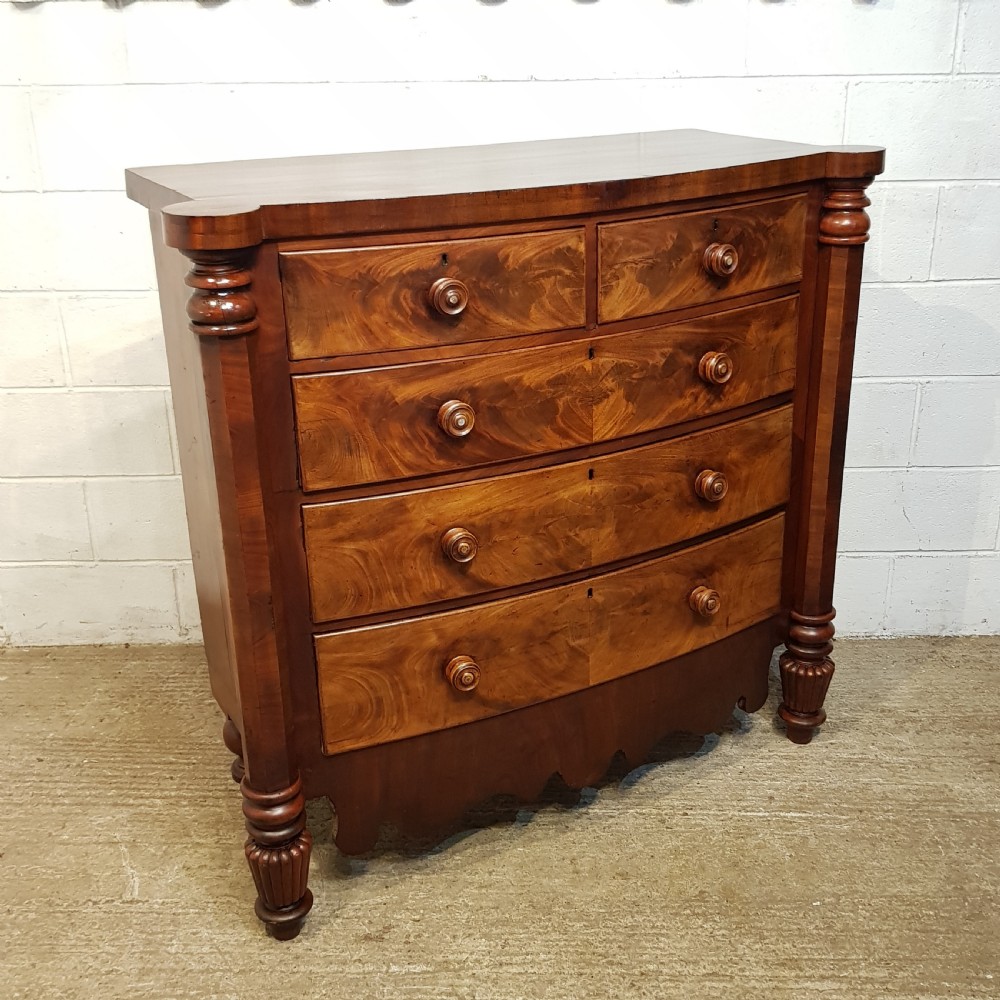 An antique Victorian bow-fronted Scotch chest of drawers featuring flame mahogany veneer, turned side columns, and turned wooden knobs. View II