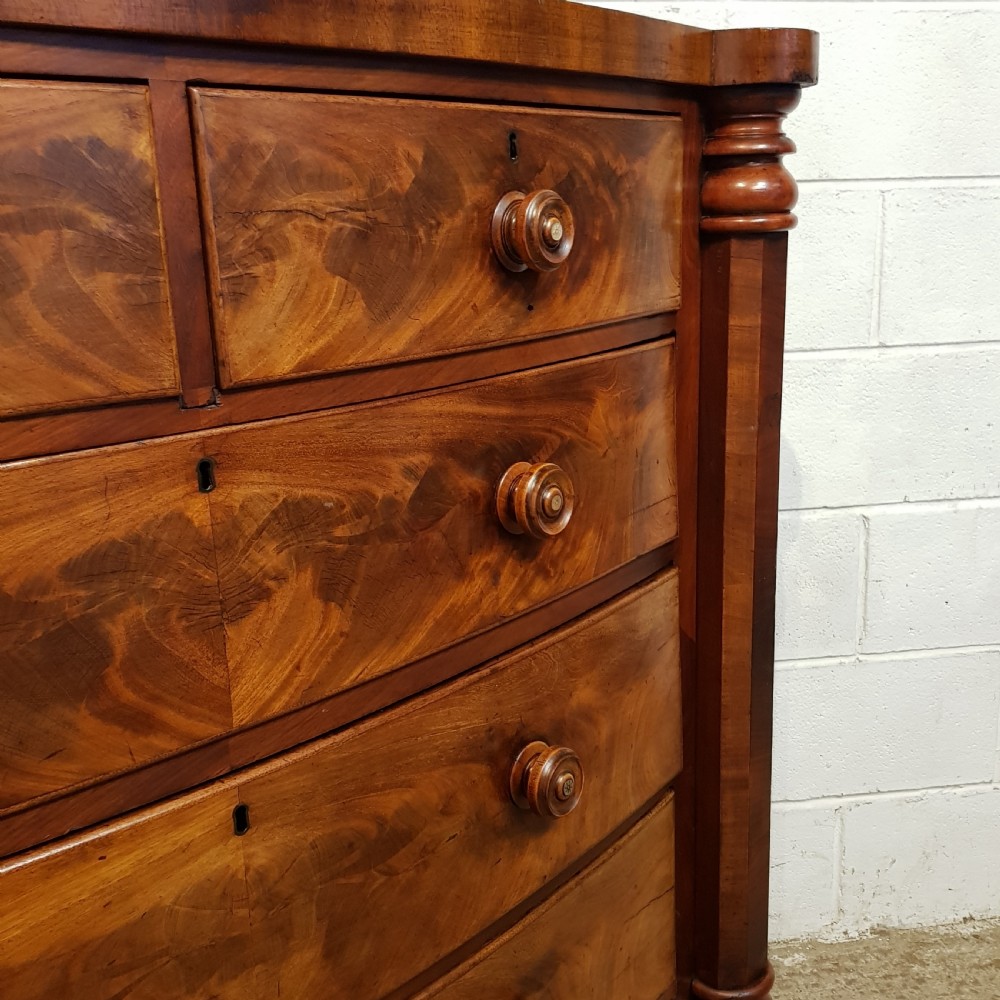 An antique Victorian bow-fronted Scotch chest of drawers featuring flame mahogany veneer, turned side columns, and turned wooden knobs. View VII