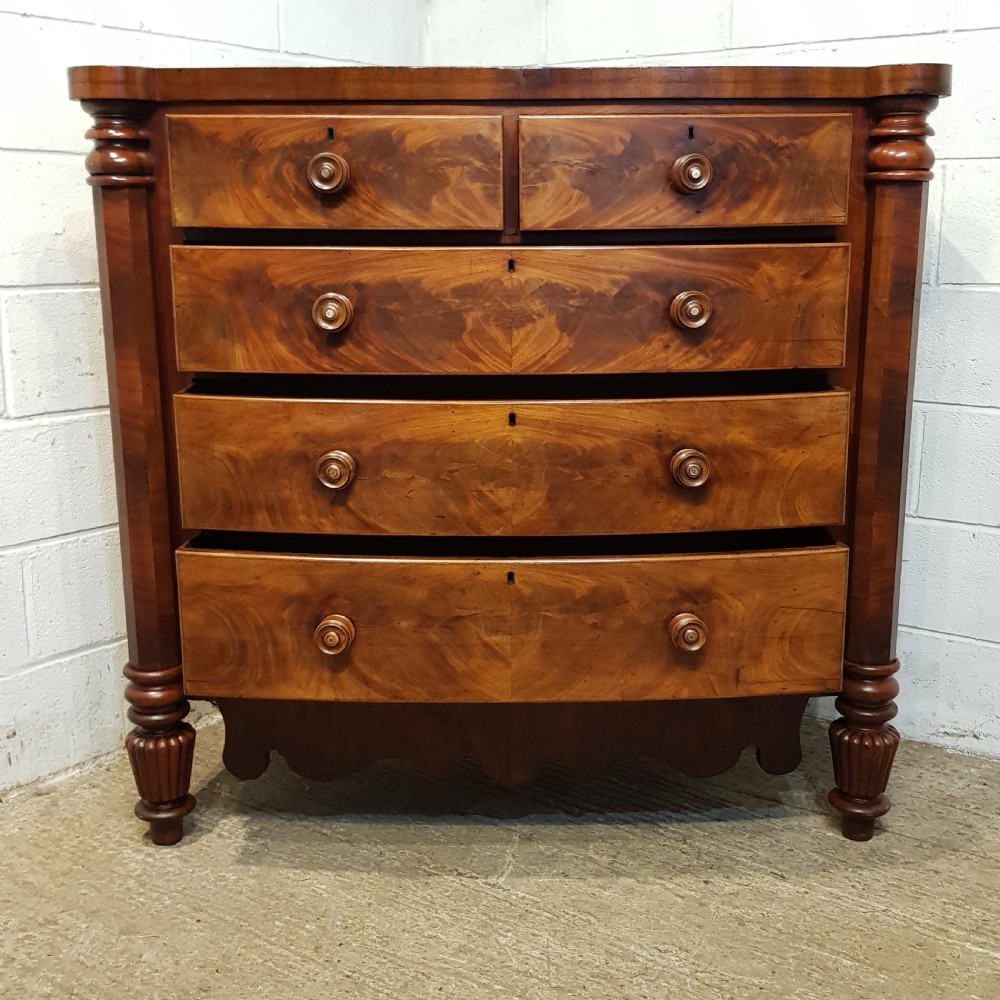 An antique Victorian bow-fronted Scotch chest of drawers featuring flame mahogany veneer, turned side columns, and turned wooden knobs. View VIII