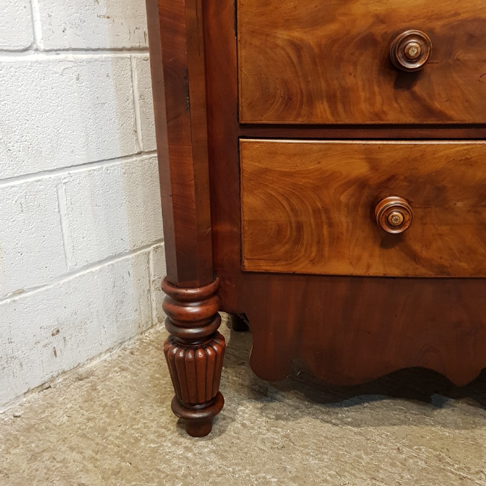 An antique Victorian bow-fronted Scotch chest of drawers featuring flame mahogany veneer, turned side columns, and turned wooden knobs. View IX