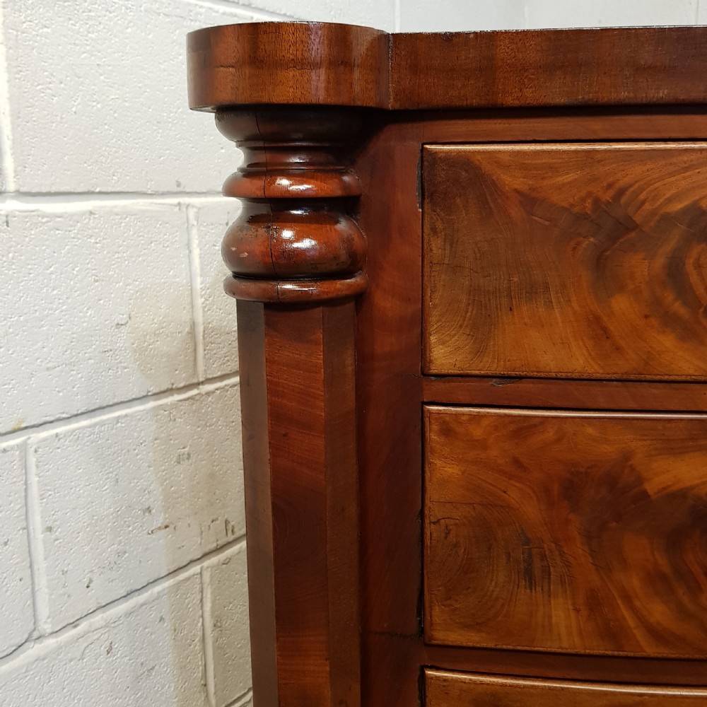 An antique Victorian bow-fronted Scotch chest of drawers featuring flame mahogany veneer, turned side columns, and turned wooden knobs. View X