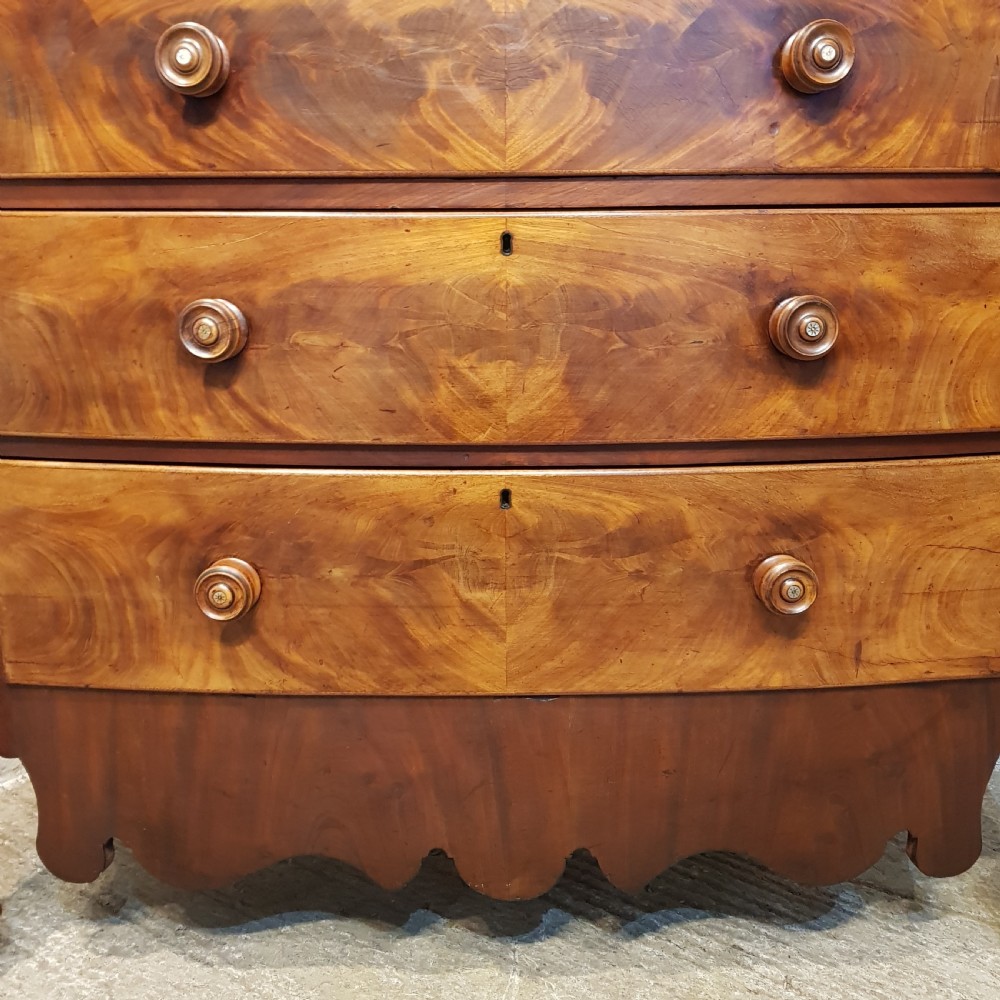 An antique Victorian bow-fronted Scotch chest of drawers featuring flame mahogany veneer, turned side columns, and turned wooden knobs. View XI
