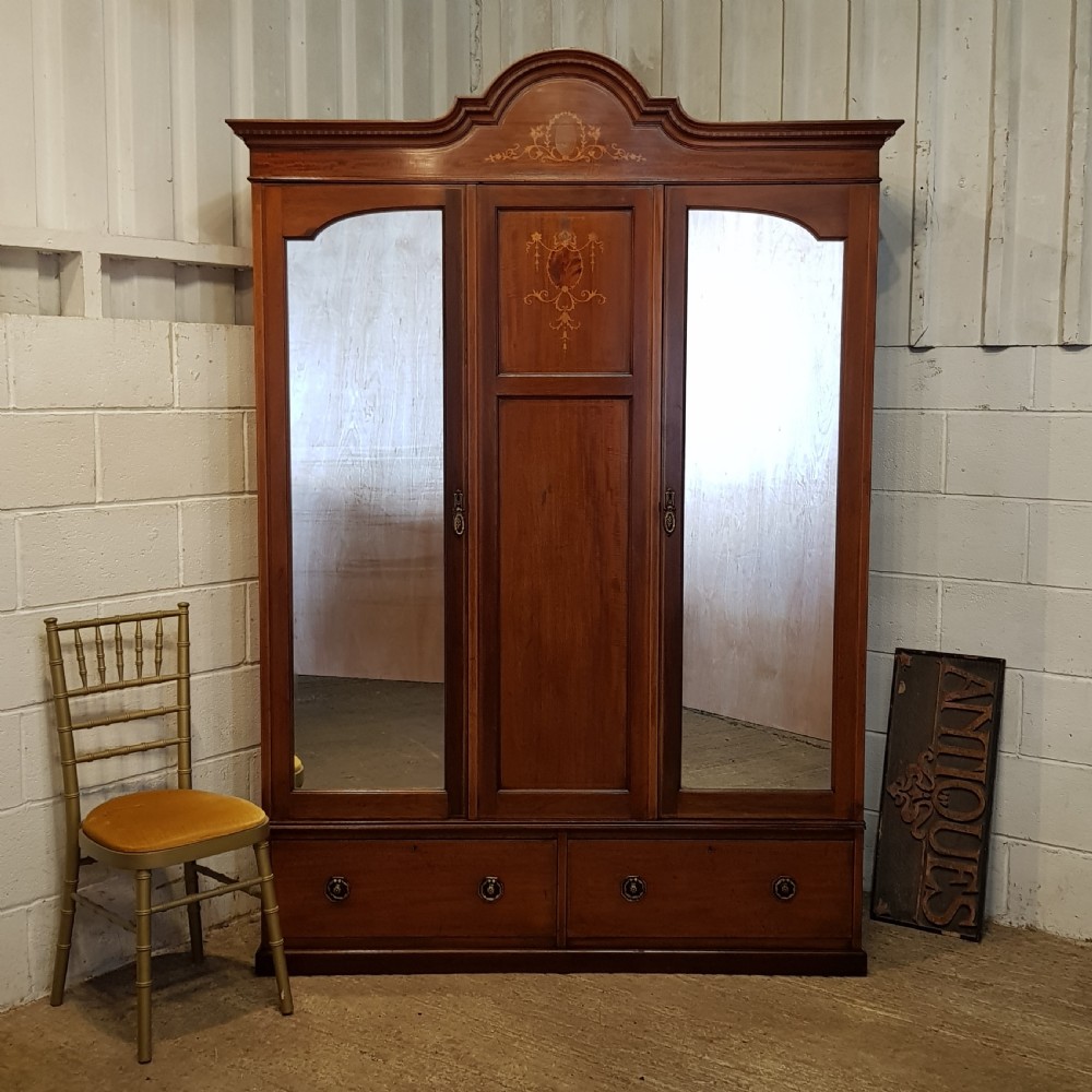 An Edwardian mahogany wardrobe with two outer mirrored doors, a central panel featuring wood inlay, and two drawers at the base.