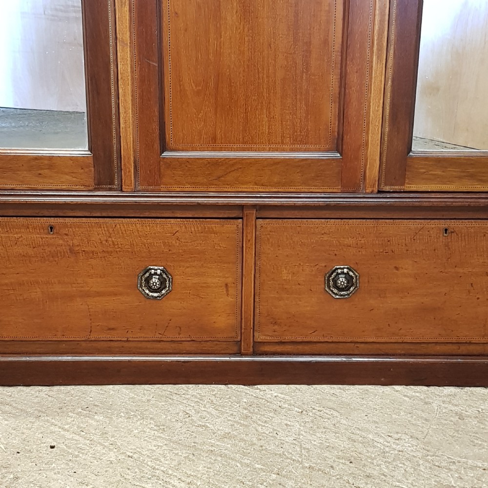An Edwardian mahogany wardrobe with two outer mirrored doors, a central panel featuring wood inlay, and two drawers at the base. View III