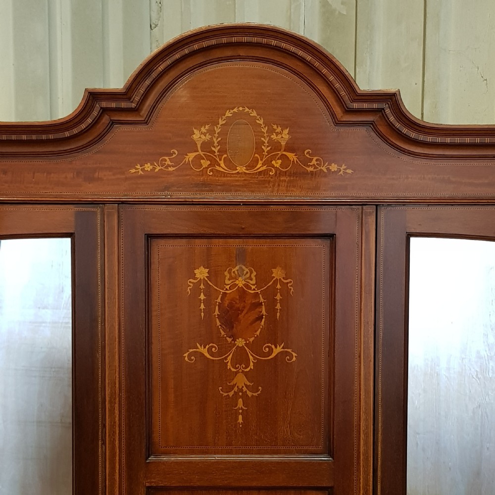An Edwardian mahogany wardrobe with two outer mirrored doors, a central panel featuring wood inlay, and two drawers at the base. View V