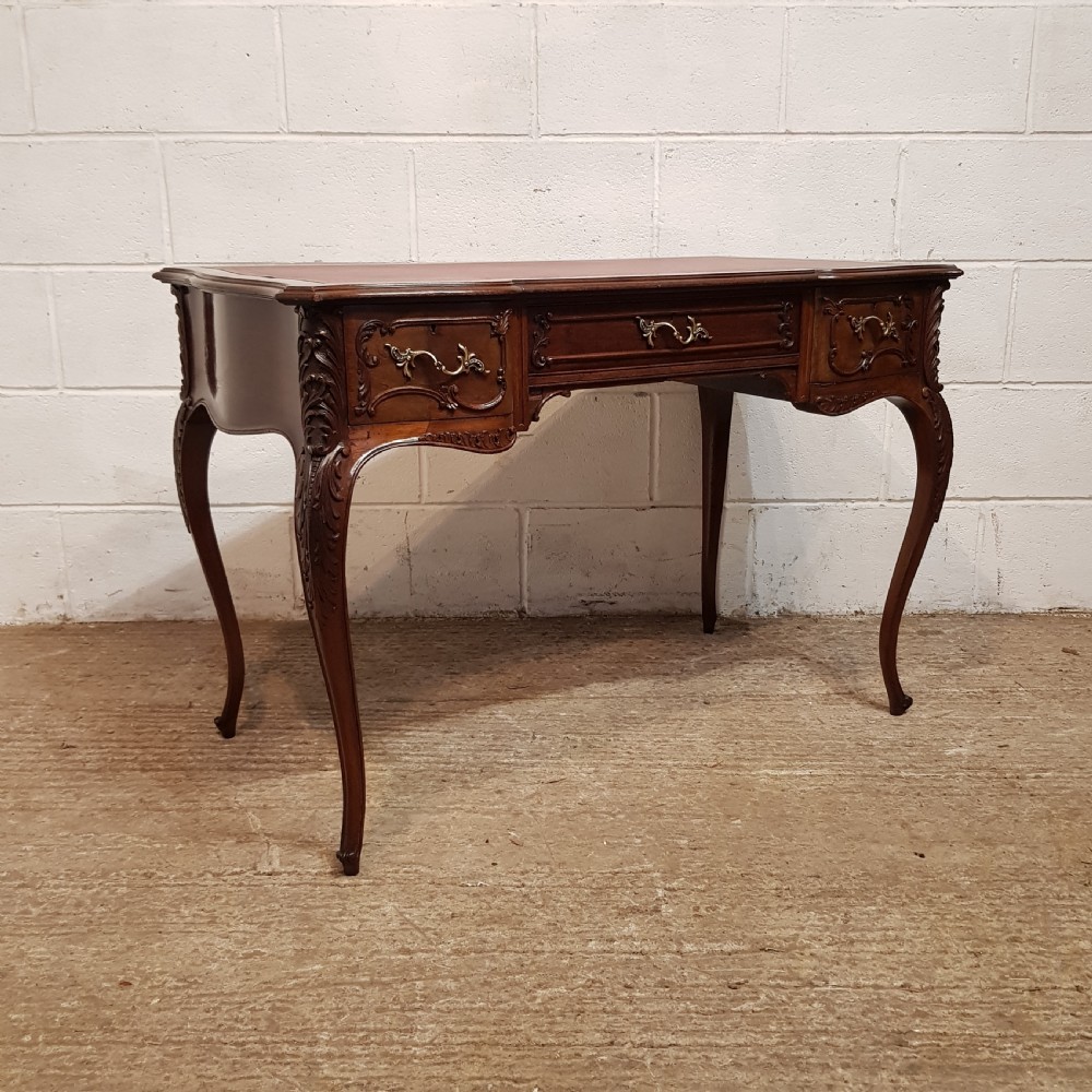 A late 19th-century French mahogany writing desk with a serpentine front, red leather inset top, three carved drawers, and slender cabriole legs. View V