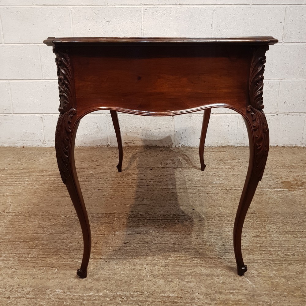 A late 19th-century French mahogany writing desk with a serpentine front, red leather inset top, three carved drawers, and slender cabriole legs. View VI