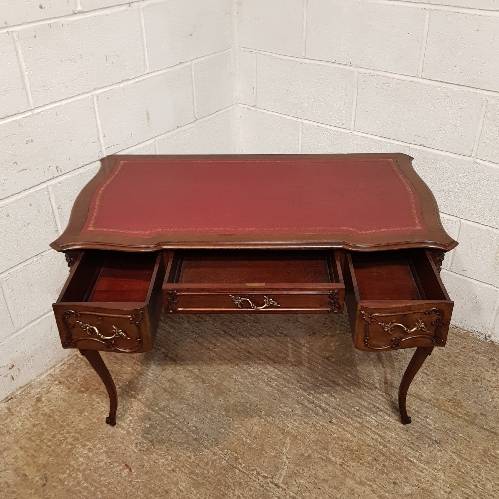 A late 19th-century French mahogany writing desk with a serpentine front, red leather inset top, three carved drawers, and slender cabriole legs. View VII