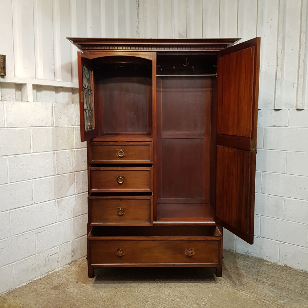 An antique Arts and Crafts mahogany combination wardrobe featuring a leaded glass cabinet, multiple drawers, copper strap hinges, and a tall mirrored door. View III