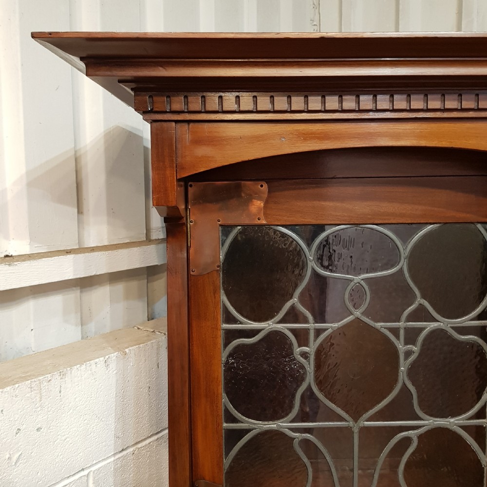 An antique Arts and Crafts mahogany combination wardrobe featuring a leaded glass cabinet, multiple drawers, copper strap hinges, and a tall mirrored door. View V